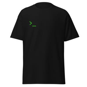 Puede incluir: Una camiseta negra de manga corta que presenta un pequeño símbolo de línea de comandos en verde brillante, compuesto por un signo de mayor que y un guion bajo, situado en la parte superior izquierda del pecho sobre la tela negra.