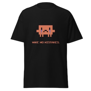 May include: A black short-sleeve t-shirt featuring a pixelated orange square character with blue teardrops and a sad expression. Below the character, the text reads "MAKE NO MISTAKES." in a matching orange pixelated font centered on the chest.