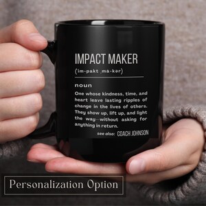 May include: A white ceramic mug with a black handle and the text "But First, Coffee" in a bold, black font. The mug is sitting on a wooden surface. The mug is approximately 4 inches tall.
