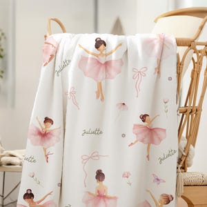Kids Ballet Theme blanket with a pattern of pink-clad ballerinas, bows, and floral motifs. The name "Juliette" is written in cursive. The blanket is draped over a wicker chair, creating a soft, feminine aesthetic.