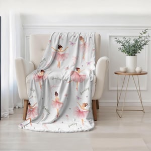 A white and pink personalized Ballet Theme Blanket is draped over a white chair in a contemporary-style room.