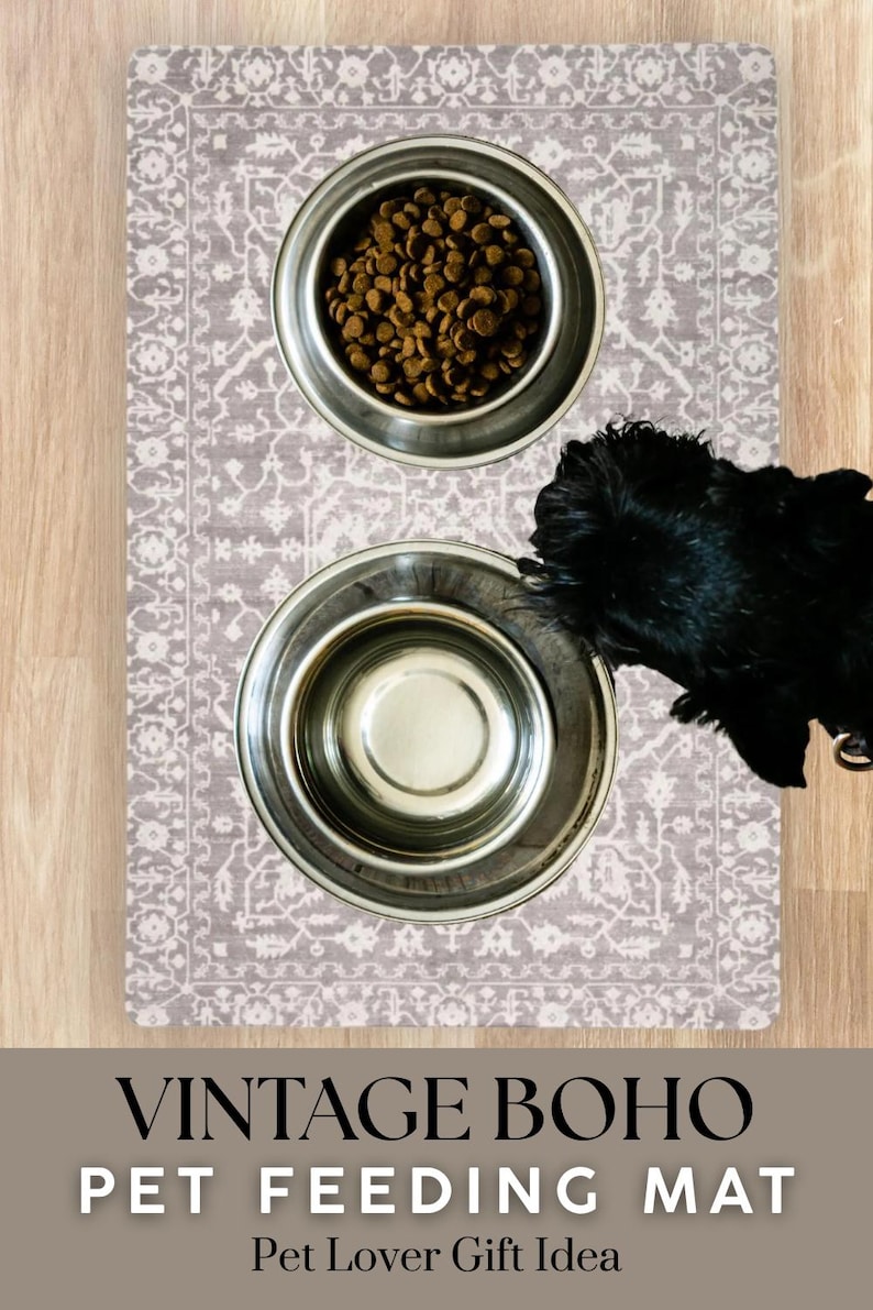 May include: A vintage boho pet feeding mat with two stainless steel bowls. One bowl is filled with dry pet food. The mat has a gray and white patterned design. A black dog is partially visible.