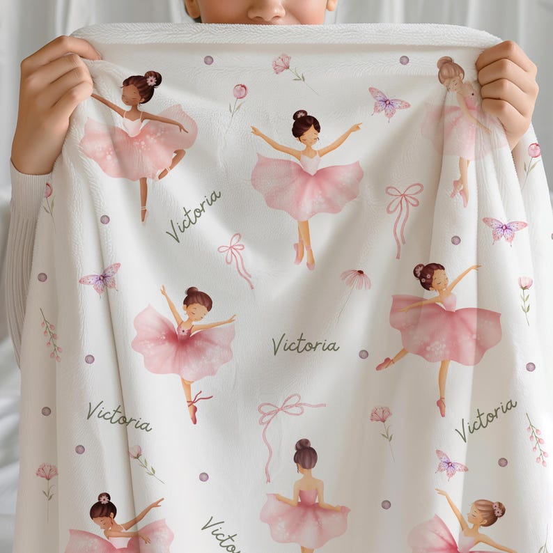 Girl holding a Dance Blanket for Girls that is Personalized with a name. The blanket features ballerinas dressed in pink tutus, bows, flowers, and butterflies.
