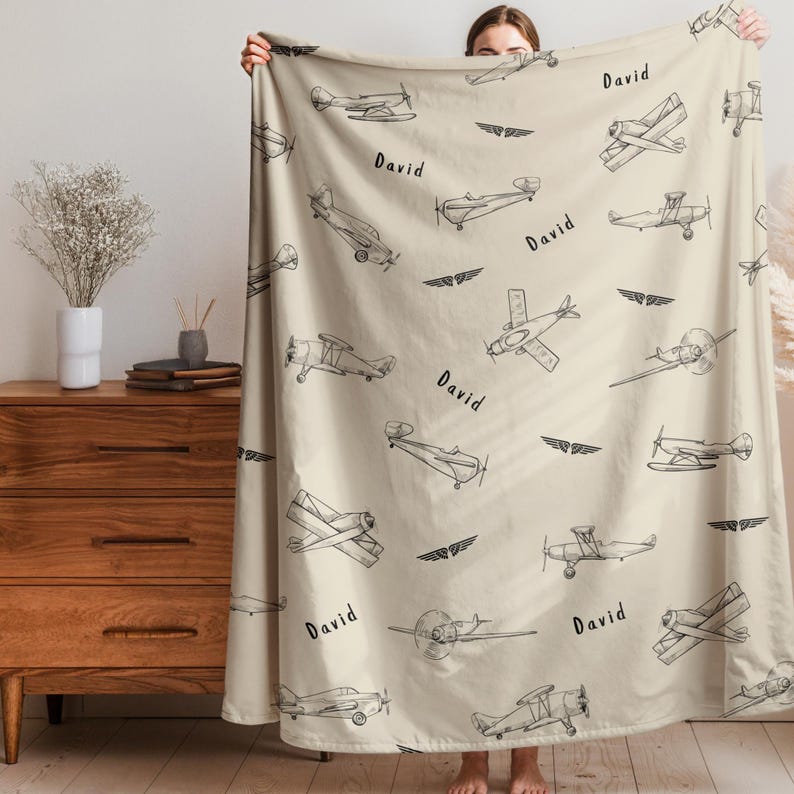 A beige Custom Name Vintage Airplane blanket with a repeating pattern of black airplane illustrations and the name "David" in a handwritten font. The blanket has a soft, cosy appearance, suitable for home decor.
