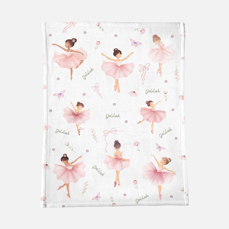 May include: White blanket featuring a pattern of pink ballerinas in various poses. The design includes butterflies, bows, flowers, and the name "Delilah" in a script font. The ballerinas wear pink tutus and have their hair in buns.