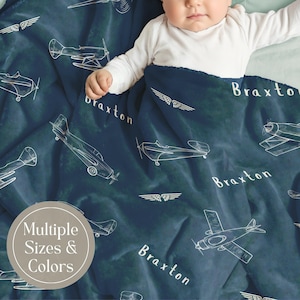 Puede incluir: Una manta de felpa azul oscuro con un patr&oacute;n repetitivo de l&iacute;neas blancas de varios aviones y el nombre Braxton impreso en una fuente blanca sin remates, con un texto superpuesto que indica Multiple Sizes & Colors.