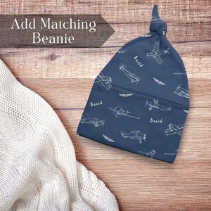 Puede incluir: Un gorro azul marino con nudo superior que presenta un patr&oacute;n de l&iacute;neas blancas de aviones antiguos y el nombre David impreso repetidamente. El gorro tiene un detalle de nudo en la parte superior y se muestra junto a una tela de punto blanca.