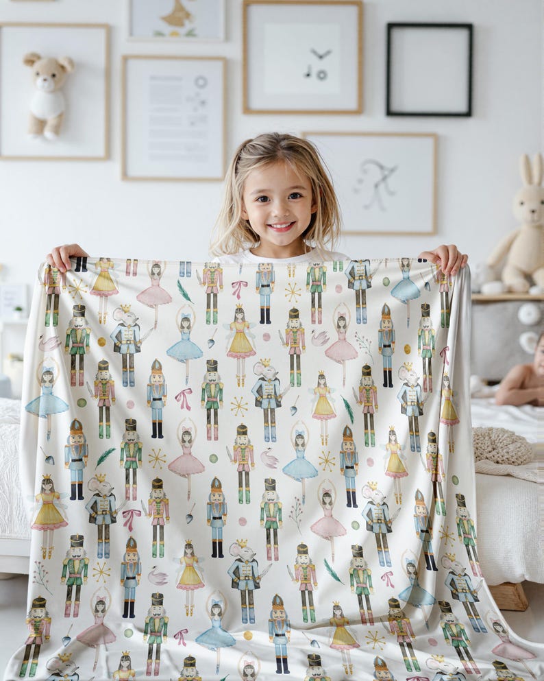 A Pink Christmas Cottagecore Throw for Her with a repeating pattern of watercolour-style nutcrackers, ballerinas, and mice. The blanket has a soft, cosy appearance, suitable for a child's bedroom. The design includes various colours such as blue, pink, yellow, and green.