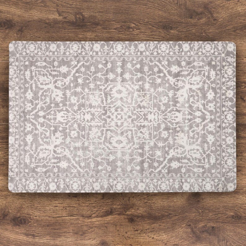 A rectangular, Grey Rug Dog Mat for Food Bowls  with a detailed, white, vintage-style pattern. The design features floral and geometric elements, creating a classic rug appearance. The placemat is set against a wooden surface.