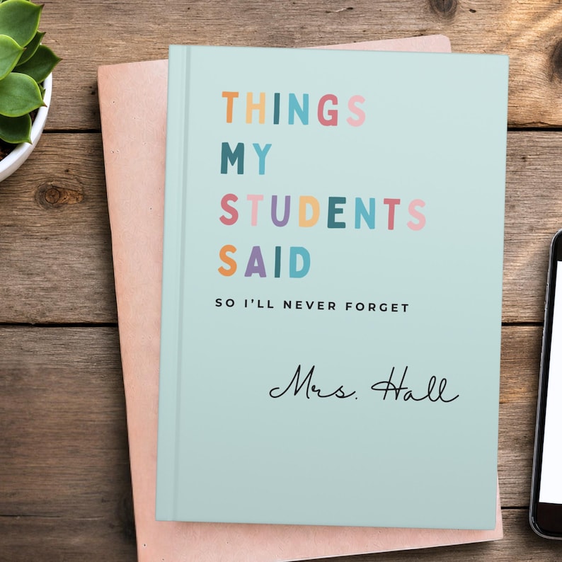 A light seafoam End of Year Teacher Appreciation Gift notebook with the text "THINGS MY STUDENTS SAID" in colourful letters. The notebook also has the text "SO I'LL NEVER FORGET" and a signature. The notebook is on top of a brown envelope.