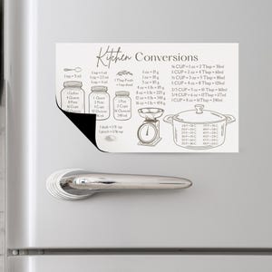 May include: A rectangular white kitchen conversion magnet featuring black text and line drawings of mason jars, a kitchen scale, and a cooking pot. The chart displays various volume, weight, and temperature measurements in metric units.