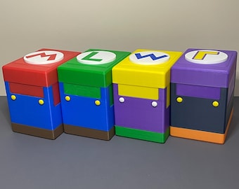 Puede incluir: Cuatro cajas de almacenamiento apiladas y coloridas, cada una con un tema de personaje diferente. Las cajas son rojas, verdes, amarillas y moradas, con detalles en azul y marrón. Cada caja tiene una tapa circular blanca con una inicial de personaje.