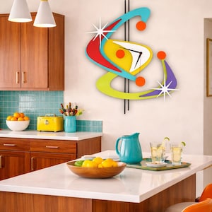 May include: A vibrant, retro-style wall clock with a starburst design. The clock has a yellow face, red and blue details, and black hands. It's mounted on a white wall in a kitchen. The kitchen has wooden cabinets.
