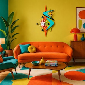 Op de afbeelding: Een wandklok in stervorm met een witte wijzerplaat en zwarte wijzers, omringd door oranje en turquoise boemerangvormige accenten, een geel zonnestraalelement en zwarte cirkelvormige markeringen in een gelaagd ontwerp.