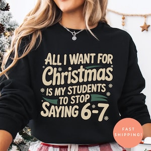 May include: Black sweatshirt with the text "ALL I WANT FOR Christmas IS MY STUDENTS TO STOP SAYING 6-7". The sweatshirt is paired with red and white plaid pajama pants. A white mug with a Santa Claus graphic is held in the hand.