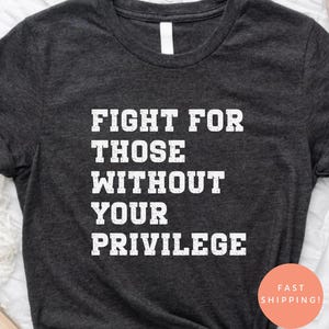 Puede incluir: Camiseta gris oscuro con el texto "FIGHT FOR THOSE WITHOUT YOUR PRIVILEGE" en letras blancas. La camiseta está anudada en la parte inferior. Una pegatina redonda con "FAST SHIPPING!" es visible.