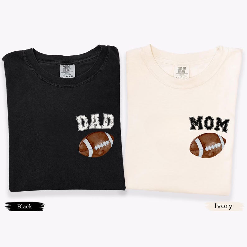 May include: Two t-shirts, one black and one ivory, each with a football graphic. The black shirt has the word "DAD" above the football, and the ivory shirt has "MOM". Both shirts are folded.