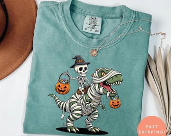 Camiseta de dinosaurio de Halloween con colores cómodos, camiseta de T-Rex con esqueleto montando momia, camiseta de dinosaurio de temporada espeluznante, linda camiseta para fiesta de Halloween, regalo de calabaza