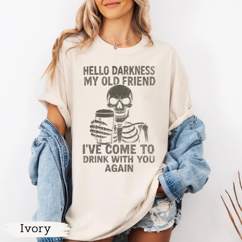 K&ouml;nnte beinhalten: Elfenbeinfarbenes T-Shirt mit dem Text "HELLO DARKNESS MY OLD FRIEND" &uuml;ber einem Skelett, das ein Bier h&auml;lt. Unter dem Skelett steht der Text "I'VE COME TO DRINK WITH YOU AGAIN".