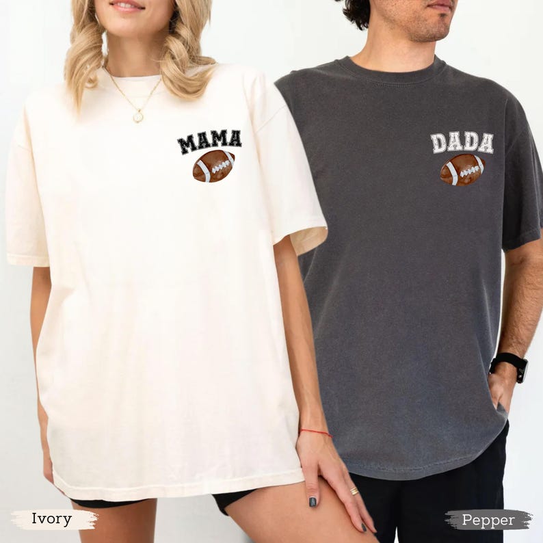 May include: Two short-sleeved t-shirts, one ivory and one pepper, featuring the words "MAMA" and "DADA" above a football graphic. The ivory shirt has a slightly oversized fit. The pepper shirt has a more fitted style.