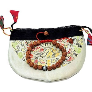 May include: A beige pouch with a black top and a colorful floral design, holding a brown beaded bracelet. The pouch has red and green tassels and a drawstring closure. The bracelet has a black and white bead.