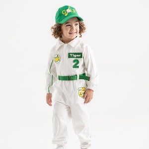May include: A child wearing a white golf-themed jumpsuit with green accents, a green belt, and a matching green cap. The cap has the word "GOLF" on it. The jumpsuit has the word "Tiger" and the number "2" on it.