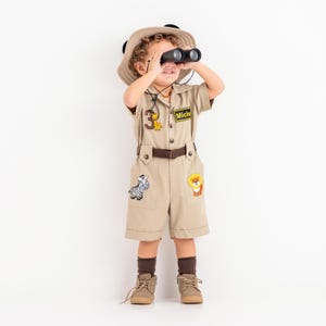 a little boy in a safari outfit looking through a pair of binoculars
