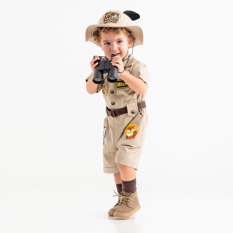 a little boy dressed in a safari outfit holding a camera