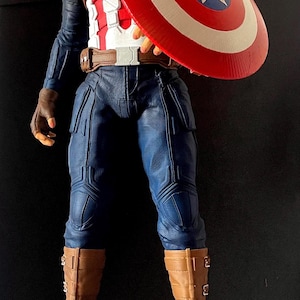 Puede incluir: Una figura de Capit&aacute;n Am&eacute;rica se encuentra sobre una base con el texto "CAPTAIN AMERICA THE FIRST AVENGER". La figura viste un uniforme azul y blanco, botas marrones y sostiene un escudo rojo, blanco y azul.