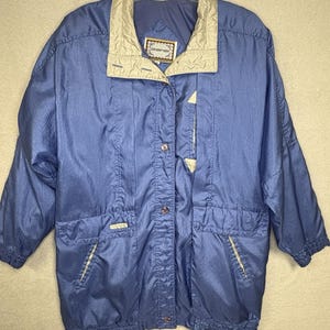 May include: A blue jacket with a beige collar and accents. The jacket has a button-up front, two front pockets, and a small label on the collar. The jacket is made of a shiny material.
