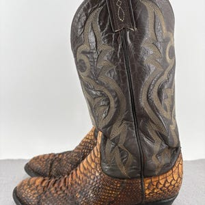 Könnte beinhalten: Ein hoher Stiefel im Western-Stil mit einem dunkelbraunen Lederschaft mit aufwendigen beigen Nähten und einem strukturierten, schuppenartigen braunen Lederfuß. Der Stiefel hat eine spitze Zehenpartie, einen Absatz und Zuglaschen am Schaft.