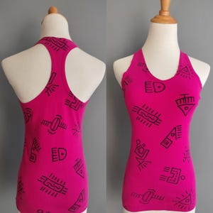 May include: A hot pink tank top with a halter neckline and racerback design. The tank top is adorned with black geometric shapes and the letters "ED". The garment is displayed on a mannequin.