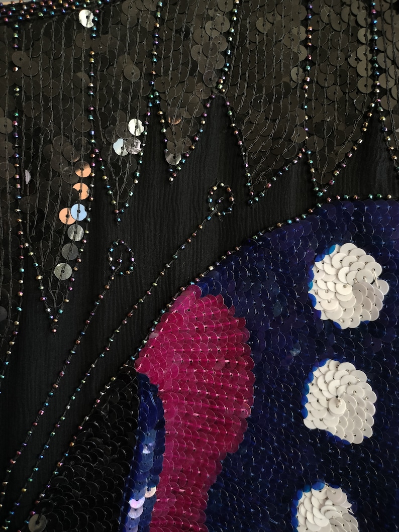 May include: A black fabric with sequins, featuring a butterfly design in shades of blue, pink, and white.