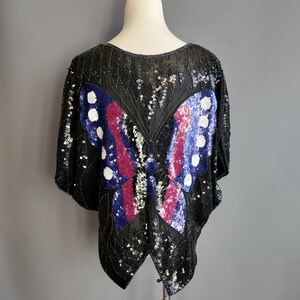 May include: A black sequined top featuring a large butterfly design in shades of blue, pink, and white.