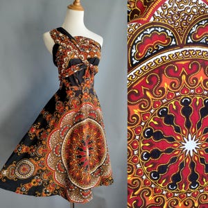 May include: A black and red one-shoulder dress with a paisley print. The dress has a fitted bodice and a flowing skirt.