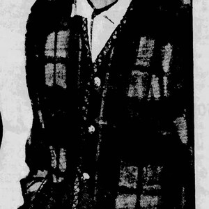 May include: A black and brown plaid cardigan sweater over a white collared shirt. The sweater has a button-up front and is worn by a person. The image is a vintage illustration.