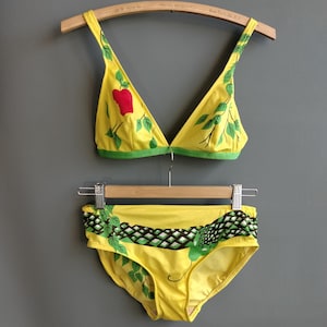 May include: Yellow bikini with a green and brown snake print on the bottom and a green and red apple print on the top.