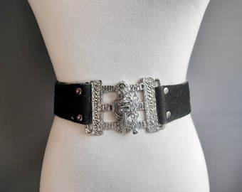 May include: A black suede belt with a large, ornate silver buckle featuring a keyhole design.