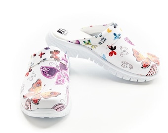 Op de afbeelding: Witte klompen met een kleurrijk vlinderpatroon. De instappers hebben een ronde neus en een textuurzool. De vlinders zijn in tinten rood, roze, paars en geel. De klompen zijn ontworpen voor comfort en stijl.