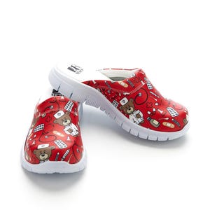 May include: Red medical clogs with a white sole. The clogs feature a repeating pattern of teddy bears in medical attire, stethoscopes, bandages, and medicine bottles. The clogs are designed for comfort and support.
