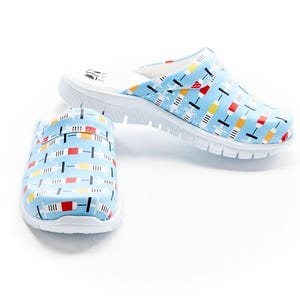 May include: Light blue clogs with a white sole and a colorful geometric pattern. The pattern includes red, yellow, and black rectangles and lines. The clogs are designed for comfort and casual wear.