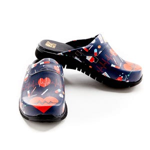 May include: Navy blue clogs with a medical theme. The shoes feature a black sole and a pattern of red hearts, pills, and EKG lines. The clogs are designed for comfort and support, suitable for healthcare professionals.