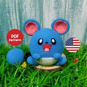 May include: A blue crochet creature with pink-lined ears, a smiling red mouth, and white eyes. A smaller blue crochet ball is also present. The text "PDF Pattern" is in a red circle. The background includes grass and a wooden surface.