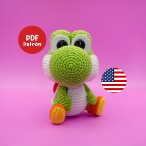 Può includere: Bambola Yoshi all'uncinetto, verde, bianca, arancione e gialla, su sfondo rosa. La bambola ha grandi occhi neri. Un cerchio rosso con il testo "PDF Patrón" è a sinistra e la bandiera americana è a destra.