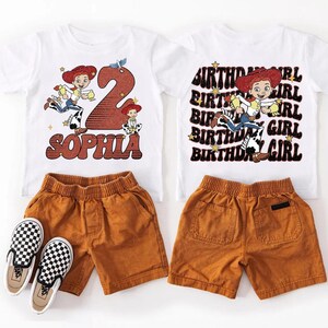 May include: Two white t-shirts with a Jessie from Toy Story graphic, paired with orange shorts and black and white checkered slip-on shoes. One shirt says "Sophia" and "2". The other says "Birthday Girl".
