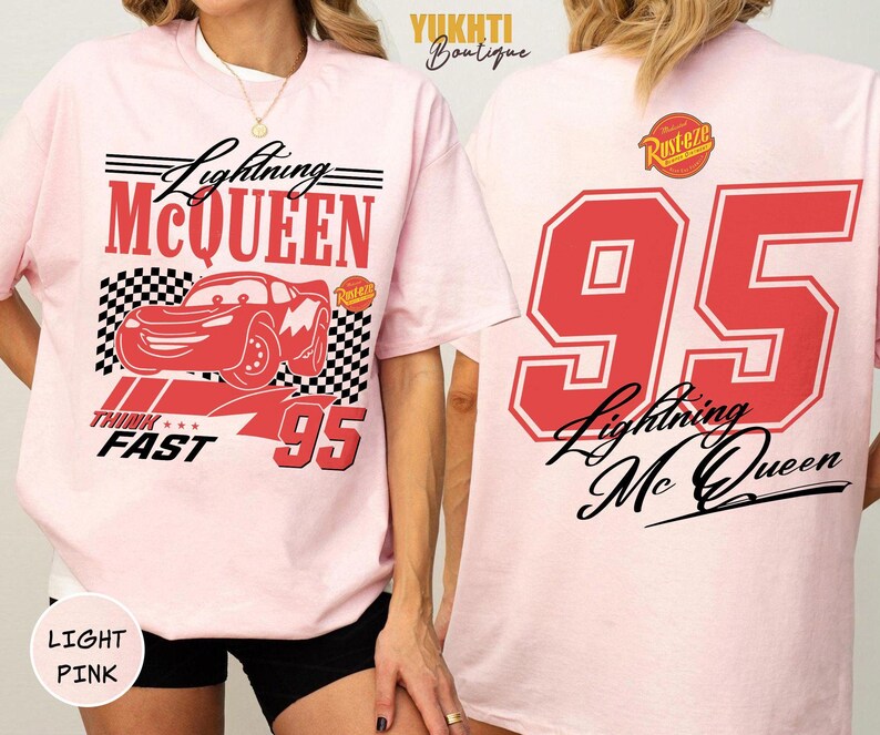 Puede incluir: Camiseta rosa claro con un dise&ntilde;o rojo de Lightning McQueen y el n&uacute;mero 95. El frente incluye "Lightning McQueen", "Think Fast" y un patr&oacute;n de bandera a cuadros. La parte trasera muestra un gran "95" rojo y "Lightning McQueen" en escritura negra.