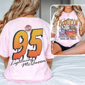 May include: Pale pink t-shirt featuring a large "95" graphic in orange and yellow on the back, with "Lightning McQueen" text. The front displays a Halloween-themed graphic with Cars characters and the words "Trick or Treat".