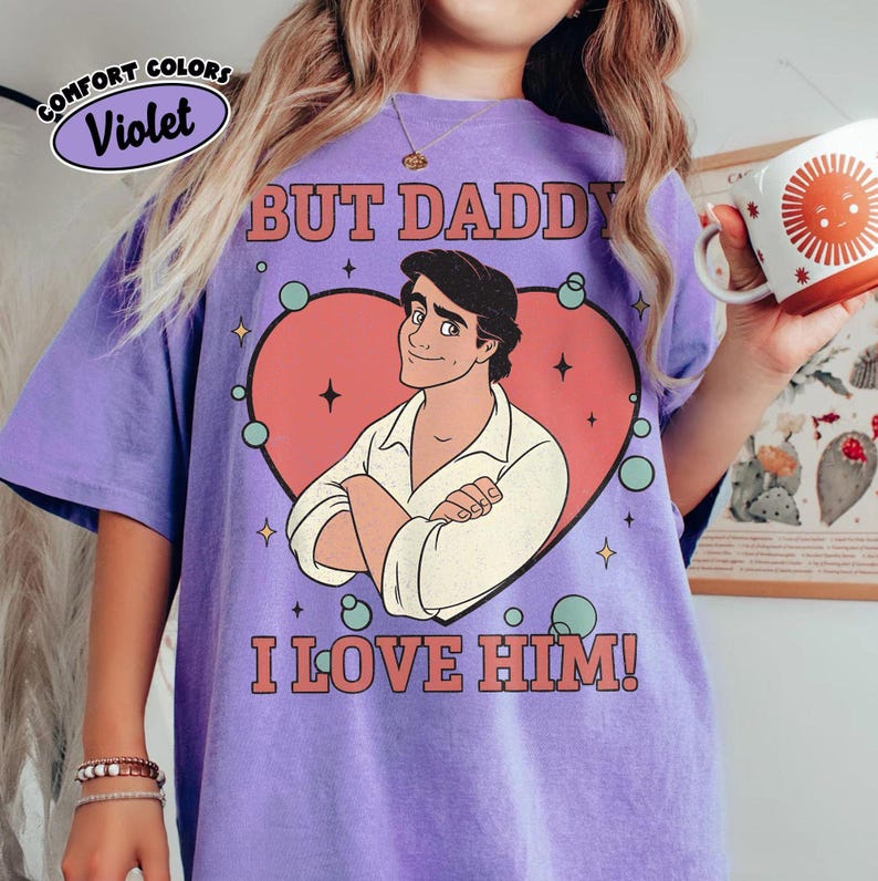 以下が含まれることがあります： バイオレットのComfort Colors Tシャツ。ハートの中に漫画の男性のグラフィックがあり、「BUT DADDY I LOVE HIM！」の文字が入っています。シャツには、円の中に「Comfort Colors」のロゴも付いています。