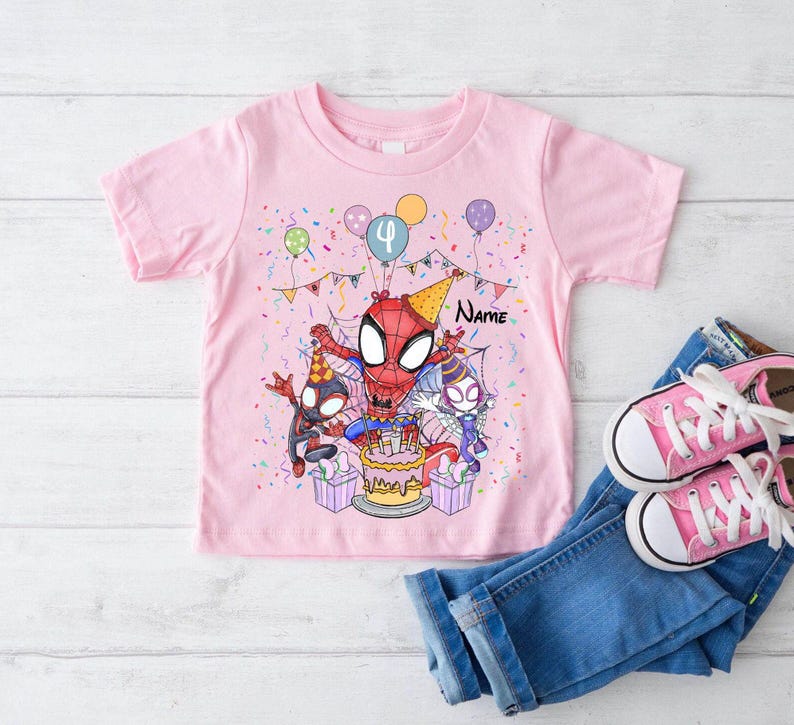 May include: Pink t-shirt featuring a Spider-Man birthday design. The graphic includes Spider-Man, a birthday cake, balloons, and confetti. The number "4" is displayed on a balloon. Blue jeans and pink sneakers are next to the shirt.