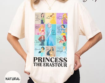 Pode incluir: Camiseta creme com um gráfico com nove ilustrações de princesas e o texto "PRINCESS THE ERASTOUR". A camisa também tem a palavra "NATURAL" impressa.